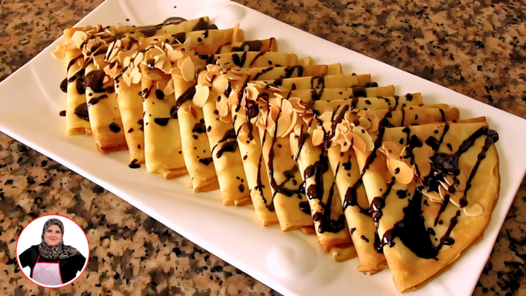 كريب على شكل مثلث مغطى بالكامل بصوص الشوكولاتة، مع قطعة فراولة مقطوعة على شكل وردة في الأعلى، موضوع على طبق أبيض.
