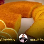 كيكة الليمون المستديرة مع شرائح برتقال مزينة في المقدمة وزهور ملونة في الخلفية.
