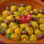 طاجين مغربي نابض بالألوان مع كرات السمك في صلصة ذهبية، مزين بالزيتون والفلفل الحلو والأعشاب الطازجة.