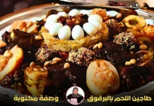 طبق طاجين البرقوق باللحم مزين بمجموعة متنوعة من المكونات مثل البيض المسلوق، الكنافة، الزبيب، واللوز المحمص، مع تقديم أنيق على صينية.