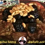 طبق مغربي تقليدي يحتوي على لحم مطهو مع البرقوق المجفف واللوز المحمص، مقدم على طبق مزخرف بزخارف شرقية.